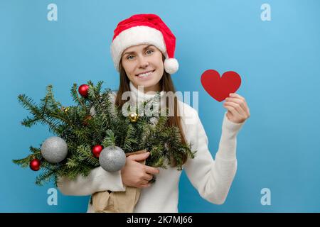 Schöne junge Frau mit kleinen roten Herzen und handgefertigten grünen Fichtenstrauß bereitet sich auf Weihnachten im Voraus genießt Neujahr, posiert über Stockfoto