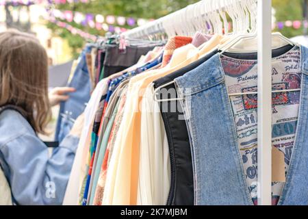 Lviv, Ukraine - September 29. 2022 : Frau auf der Suche nach Vintage-Kleidung auf dem Flohmarkt. Kleidung an Kleiderbügeln - Second Hand Bekleidungsgeschäft oder Sparsamkeit shoppi Stockfoto