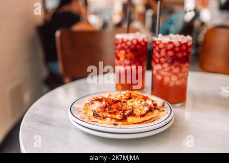 Spanische Vorspeise im Fischrestaurant in Valencia, gegrillter Oktopus mit gerösteten Kartoffeln und Paprika, Spanien. Kalter Sangria-Drink-Cocktail auf dem Hintergrund Stockfoto