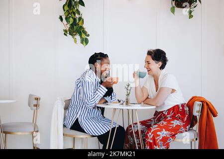 Fröhliche Geschäftsfrauen, die lachen und gemeinsam in einem Bürocafé Kaffee trinken. Zwei glückliche Geschäftsfrauen genießen gemeinsam eine Kaffeepause in einem modernen Wor Stockfoto