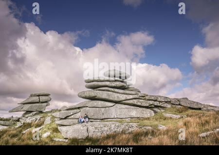 Ein junges Paar, das sich unter einem hoch aufragenden Granitfelsen-Stapel auf dem Stowes Hill auf Bodmin Moor in Cornwall entspannt. Stockfoto