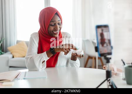 Muslimische Bloggerin nutzt Smartphone und nimmt Video für Beauty-Blog auf und zeigt Hautpflegeprodukte der Kamera Stockfoto