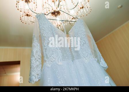 Das perfekte Hochzeitskleid mit einem vollen Rock auf einem Kleiderbügel in das Zimmer der Braut mit blauen Vorhängen Stockfoto