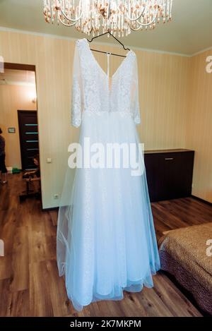 Das perfekte Hochzeitskleid mit einem vollen Rock auf einem Kleiderbügel in das Zimmer der Braut mit blauen Vorhängen Stockfoto