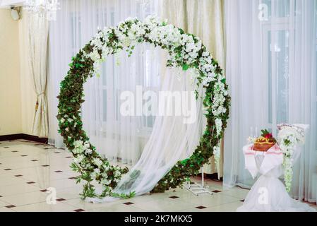 Hochzeitszeremonie. Sehr schöner und stilvoller Hochzeitbogen, geschmückt mit verschiedenen frischen Blumen, im Garten stehend. Hochzeitstag. Frische Blumen de Stockfoto