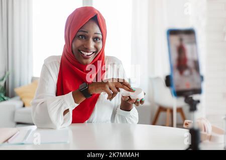 Professionelle schwarze muslimische Beauty-Blogger Werbung Hautpflege Kosmetik, im Gespräch mit Smartphone auf Stativ Stockfoto
