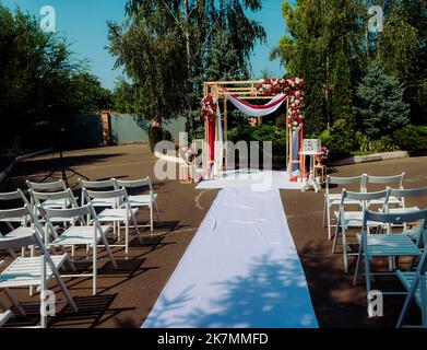 Hochzeitszeremonie. Sehr schöner und stilvoller Hochzeitbogen, geschmückt mit verschiedenen frischen Blumen, im Garten stehend. Hochzeitstag. Frische Blumen de Stockfoto