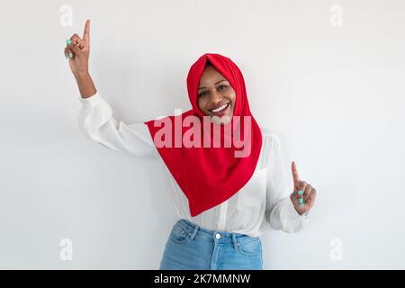 Unterhaltung für muslimische Frauen Konzept. Aufgeregte afroamerikanische islamische Frau, die Spaß hat und mit erhobenen Händen tanzt Stockfoto