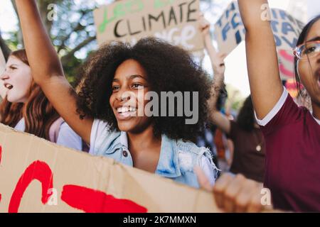 Glückliche junge Menschen, die sich gegen den Klimawandel und die globale Erwärmung einsetzen. Eine Gruppe multikultureller Jugendaktivisten marschiert mit Plakaten. Junge Leute Stockfoto