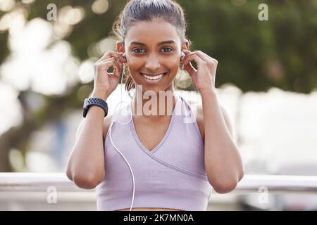 Ich kam heraus, um einige Zeit auf die beste Weise zu genießen. Porträt einer sportlichen jungen Frau, die Kopfhörer trägt, während sie im Freien trainiert. Stockfoto