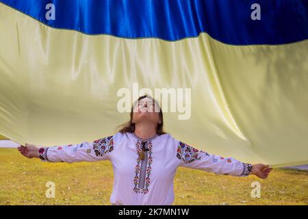 Eine junge Frau hält die Flagge der Ukraine, die ihren Kopf zum Himmel hebt, während sie für die Ukraine betet Stockfoto