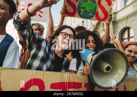 Gruppe glücklicher Klimaaktivisten protestiert mit Transparenten und einem Megaphon. Fröhliche junge Menschen marschieren gegen die globale Erwärmung und Umweltverschmutzung. Multiet Stockfoto