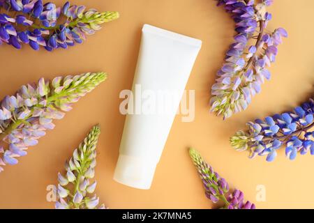 Weiße Creme-Tube und Lupine-Blüten auf goldgelbem Hintergrund. Kosmetische Hautpflege Produkt blank Kunststoff-Paket. Weiße Flasche mit nicht gebrandeter Lotion, Kal Stockfoto