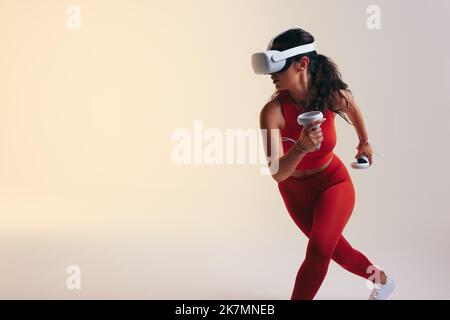 Aktive junge Sportlerin Frau läuft in der virtuellen Realität. Athletische junge Frau, die mit 3D-Technologie trainiert. Sportliche junge Frau trägt eine virtuelle Stockfoto