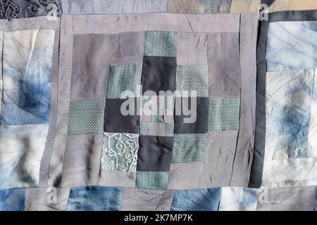 Fragment von handgefertigtem Patchwork-Quilt aus Stücken verschiedener Seidenstoffe, die in Konvergenztechnik genäht wurden Stockfoto