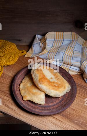 Tonplatte mit zwei einzelnen gebratenen Pasteten mit Fleisch auf Holztisch. Tatarische traditionelle Pasteten. Stockfoto