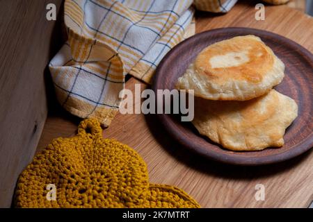 Tonplatte mit zwei einzelnen gebratenen Pasteten mit Fleisch auf Holztisch. Tatarische traditionelle Pasteten. Stockfoto