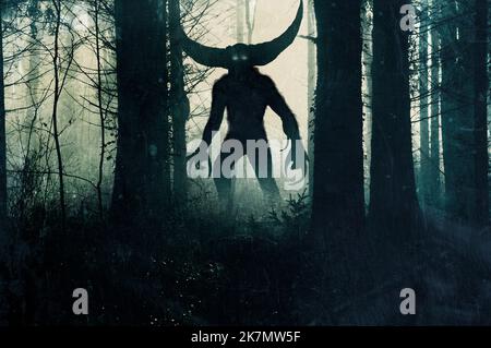 Ein dämonisches Horrormonster. Mit leuchtenden Augen und Hörnern. Silhouetten in einem dunklen, nebligen Winterwald. Stockfoto