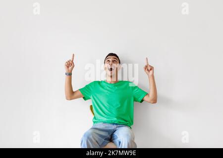 Aufgeregter arabischer Mann, der auf den Kopierraum zeigt und aufschaut, öffnet den Mund schockierend auf den hellen Hintergrund der Studiowand Stockfoto