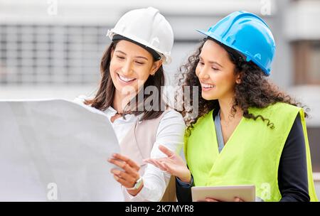 Sehen Sie sich diese Pläne an. Zwei attraktive junge Ingenieurinnen, die auf einer Baustelle stehen und Baupläne betrachten. Stockfoto