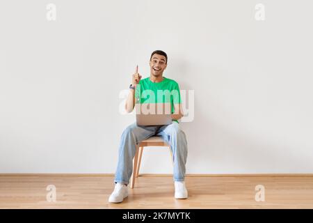 Inspirationskonzept. Aufgeregter arabischer Mann mit Laptop, der eine tolle Idee hatte, mit dem Finger nach oben zeigte und lächelte und auf einem Stuhl saß Stockfoto