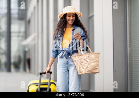 Hübsche junge Frau, die Urlaub macht, am Flughafen läuft, Smartphone benutzt Stockfoto