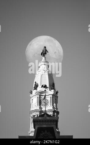 Der weiße Vollmond, der hinter der William Penn-Statue auf dem Rathaus von Philadelphia in Philadelphia, Pennsylvania, zu sehen ist Stockfoto