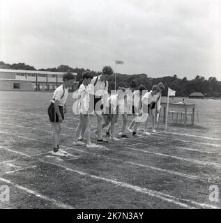 1960s, historisch, draußen auf einem Sportplatz, stellt sich eine Gruppe von Schülern am Start eines Laufrennens auf einer bemalten Strecke auf dem Rasen in der Halton School, Buckinghamshire, England, Großbritannien, ein. Alle tragen Shorts und Tops, die meisten sind in Turnschuhen, wobei einer Laufschuhe trägt, die als Spikes bekannt sind, und einer nur seine Socken trägt. Stockfoto