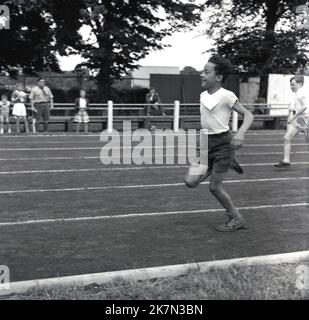 1960s, historisch, draußen auf einer Schlackenbahn, zwei junge Jungen, die an einem Sprint-Rennen teilnehmen, England, Großbritannien. Der führende Junge läuft in seinen Schulsandalen. Stockfoto