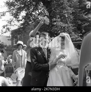 1960s, historisch, eine Dame, die das traditionelle Konfetti - Papierschnitte - über ein gerade verheiratetes Paar streut, während sie zusammen neben ihrem Hochzeitswagen stehen, England, Großbritannien Stockfoto
