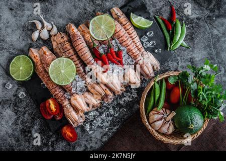 Ein Blick von oben auf rohe Mantis Garnelen, Limettenscheiben, Knoblauch und Paprika auf einem Tisch Stockfoto