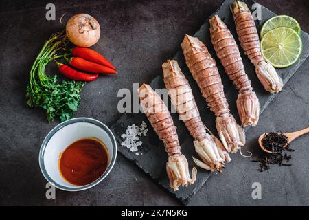 Ein Blick von oben auf rohe Mantis Garnelen, Limettenscheiben, Knoblauch, Paprika und Sauce auf einem Tisch Stockfoto