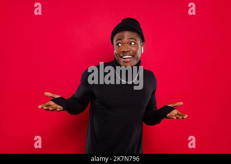 Foto von lustig unsicher jungen Kerl tragen schwarz Rollkragenkopfbedeckung Musik hören suchen leeren Raum isoliert roten Hintergrund Stockfoto