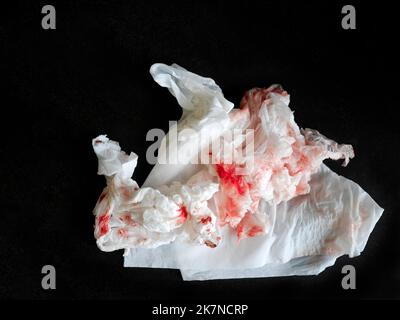 Draufsicht auf frisches rotes Blut, das auf Seidenpapier angefärbt ist, isoliert auf dunklem Hintergrund, gebrauchtes zerknittertes Wischpapier, Anschnitt, Kopierraum Stockfoto