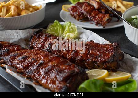 Gegrilltes Schweinefleischgericht mit frisch gegrillten Spareribs, hausgemachten pommes frites und Salat auf einem Esstisch Stockfoto