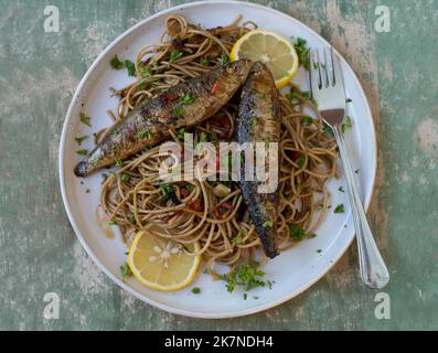 Gebratene Sardinen mit Vollkornpasta, gekocht mit Olivenöl, Knoblauch, Paprika und Petersilie auf einem Teller Stockfoto