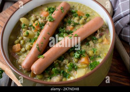 PEA-Eintopf mit wiener Wurst in einer altmodischen Schüssel auf Holzhintergrund Stockfoto