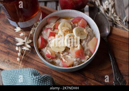 Frühstücksbrei mit Bananen, sautierten Äpfeln, Mandeln und Ahornsirup Stockfoto