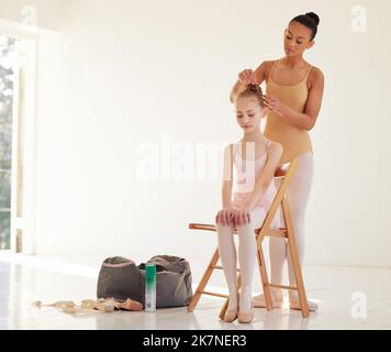 Hoffen Sie auf das Beste, bereiten Sie sich auf das Schlimmste vor. Eine Ballerina hilft einem jüngeren Mädchen, ihr Haar in einem Tanzstudio zu stylen. Stockfoto