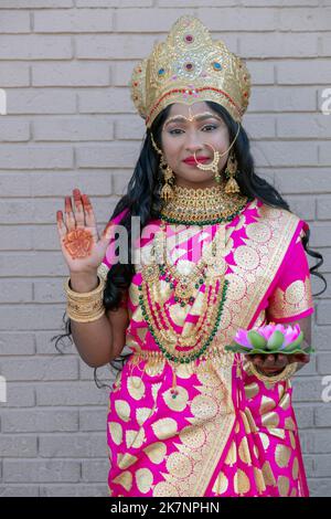 Eine attraktive Hindu-Frau, gekleidet als Lakshmi, trägt eine Krone und hält eine Lotusblume. Bei der Diwali-Feier 2022 in Queens, New York City. Stockfoto