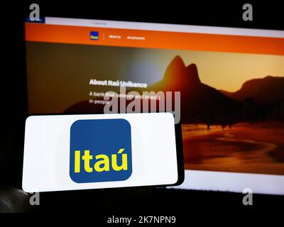 Person, die Mobiltelefon mit Logo der brasilianischen Firma Itau Unibanco Holding SA auf dem Bildschirm vor der Business-Webseite hält. Konzentrieren Sie sich auf die Telefonanzeige. Stockfoto