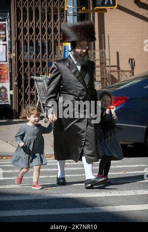 Ein haasdischer Mann mit hohen weißen Socken und einem Shtreimel geht mit seinen 2 Töchtern auf der Lee Avenue in Williamsburg. Stockfoto