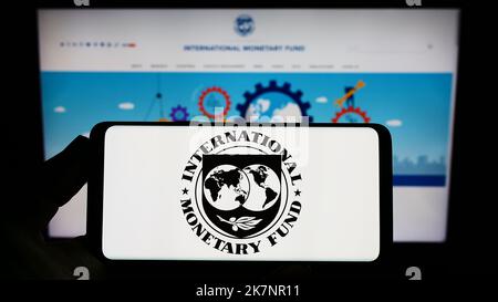 Person, die das Smartphone mit dem Logo der UN-Agentur International Monetary Fund (IWF) auf dem Bildschirm vor der Website hält. Konzentrieren Sie sich auf die Telefonanzeige. Stockfoto