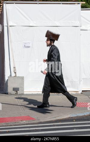 Ein chassidischer jüdischer Mann geht an einer Sukkah vorbei, die einen Shtreimel-Pelzhut trägt. In Brooklyn, New York City. Stockfoto