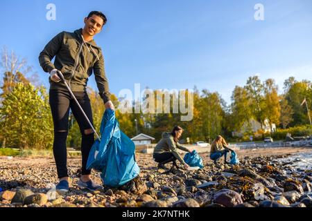 Mann, der am sonnigen Tag mit einer Gruppe von Freiwilligen den Strand putzt Stockfoto