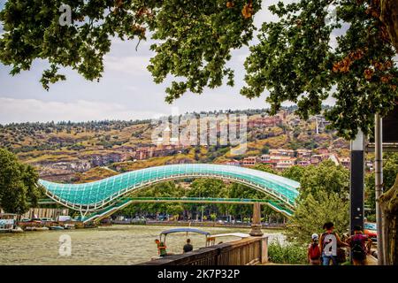 07 19 2019 Tiflis Georgien - Panoramablick auf die Friedensbrücke mit Seilbahnen, die zur Festung Narikala fahren und Booten und Bootsleuten auf dem Fluss Stockfoto