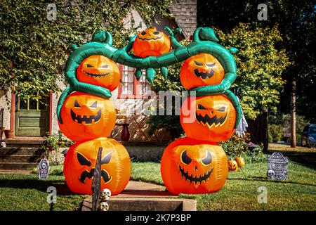 Riesiger aufblasbarer Halloween Jack-o-Laterne Torbogen vor einem niedlichen Haus mit lustigen Grabsteinen und Totenköpfen in grüner Nachbarschaft Stockfoto