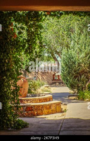 Rustikaler Innenhof von Santa Fe mit Brunnen, eingerahmt von lehmziegeltüren mit Weinreben Stockfoto