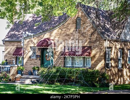 Gruseliges Vintage Cottage mit Markisen ist für Halloween mit Skeletten geschmückt, die auf dem Dach krabbeln und einem riesigen Spinnennetz Stockfoto