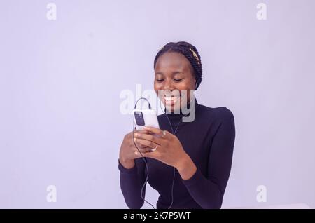 Aufgeregte afrikanische Dame isoliert auf weißem Hintergrund Musik auf ihrem Telefon hören Stockfoto